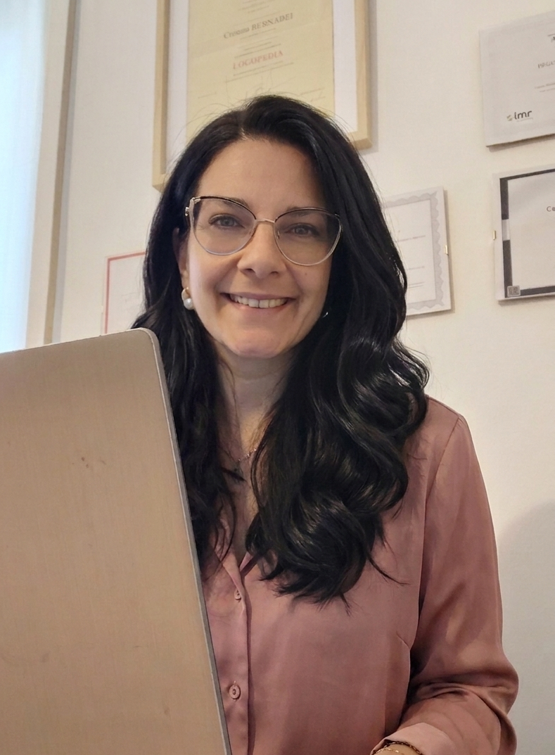 Cristina Bernabei, logopedista, donna sorridente con capelli scuri, occhiali e camicia rosa